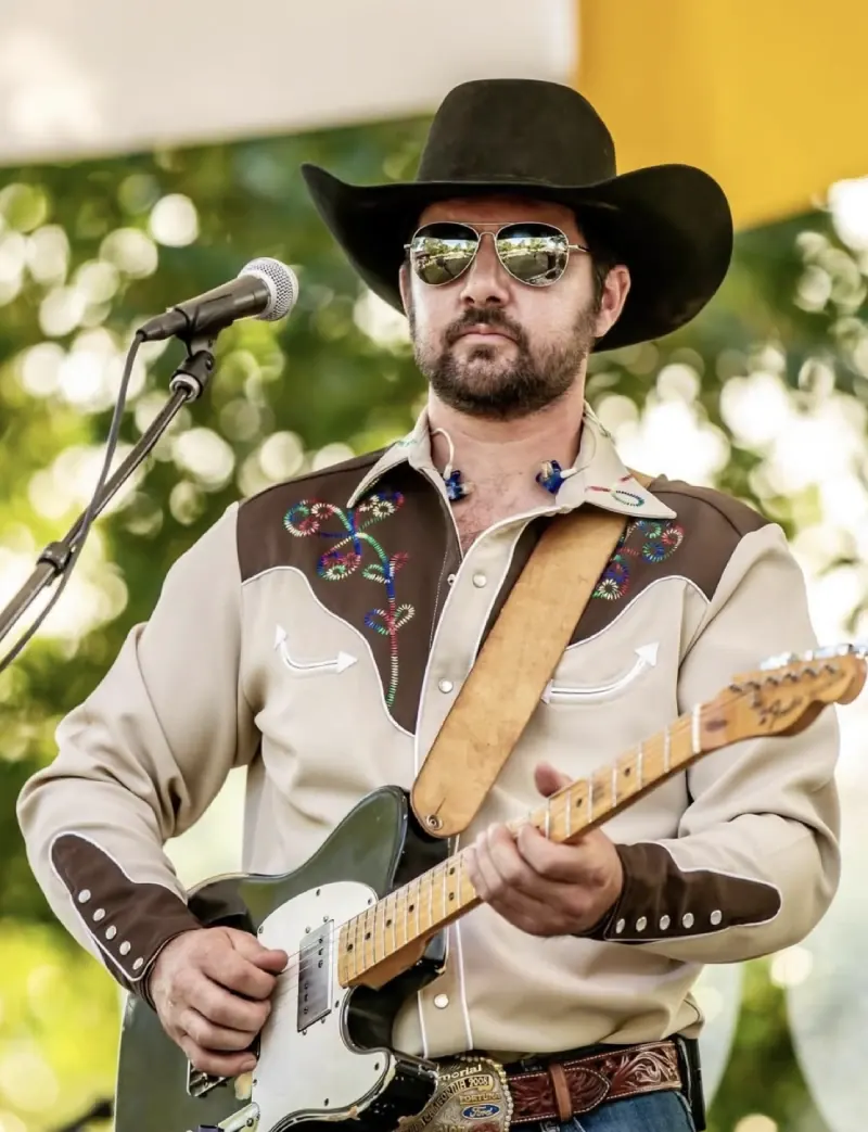 Chad Bushnell of Thunder Rolls in a cowboy hat and western shirt playing electric guitar outdoors