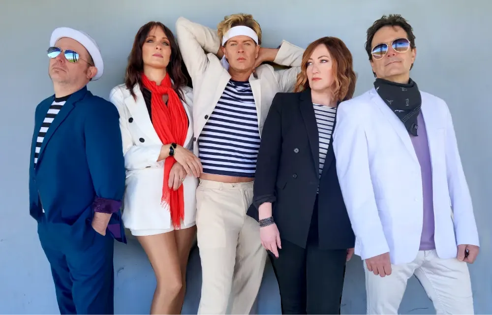 New Moon on Monday Duran Duran tribute band in white and navy outfits posing against a grey wall
